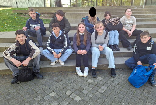 Zehn Kinder der Sekundarstufe sitzen auf einer Treppe und schauen in die Kamera