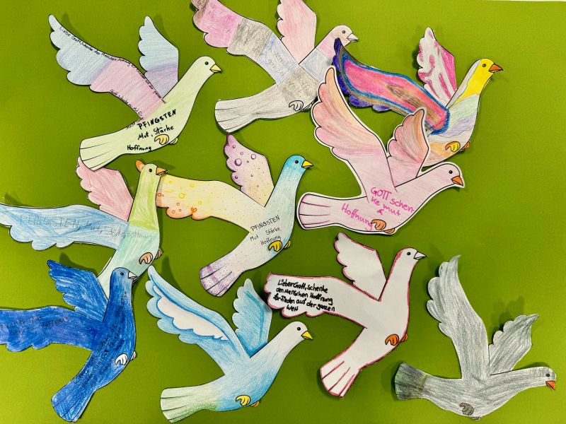 Auf dem Foto sind viele Tauben als Symbol/ Zeichen für den Heiligen Geist zu erkennen. Die Schüler:innen malten die Tauben bunt aus und schrieben: "Pfingsten - Mut, Stärke, Hoffnung" hinein.